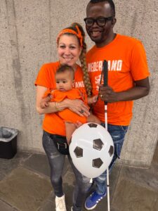 Nikki and Samy Vez posing with baby Aza in matching orange Netherlands shirts.