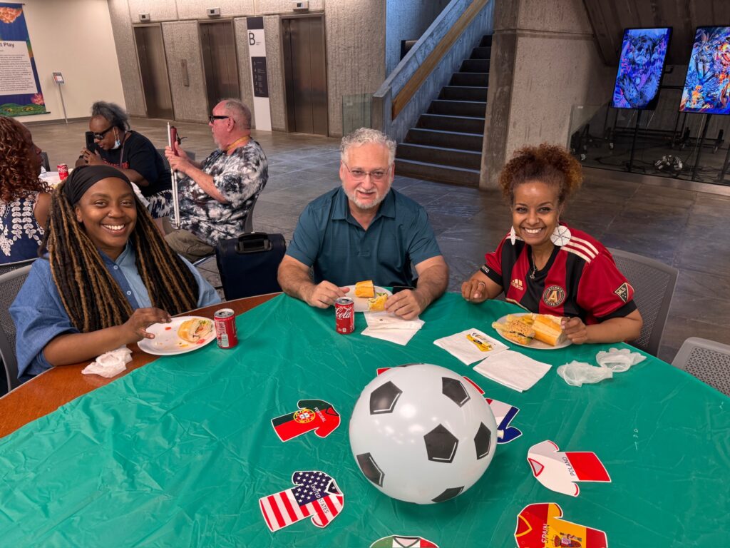 Three participants smiling together over a World Cup-themed table decorated with a soccer ball and country flags.