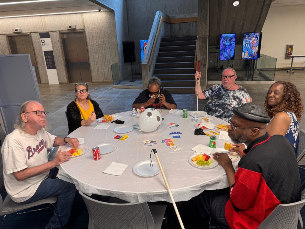 Blind and visually impaired participants sharing a meal around a World Cup-themed table, with white canes visible