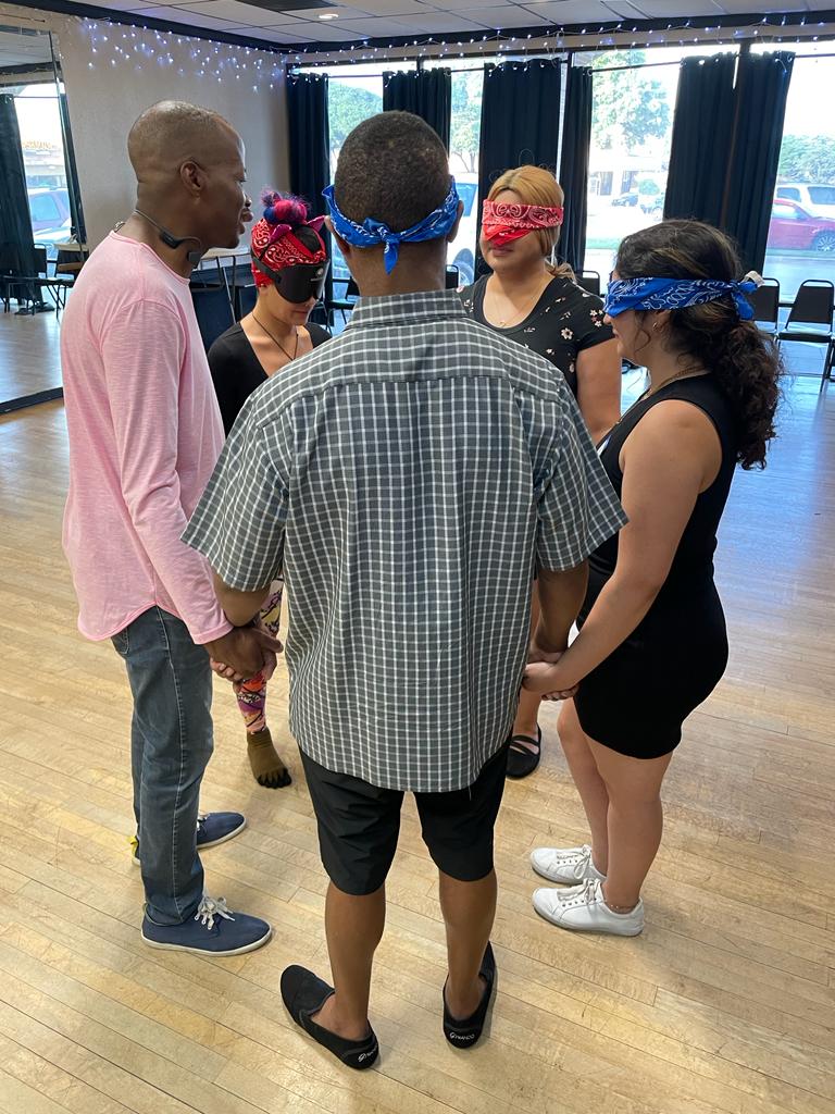 Participants, some wearing blindfolds, stand together in a circle during a Dance in the Dark workshop.
